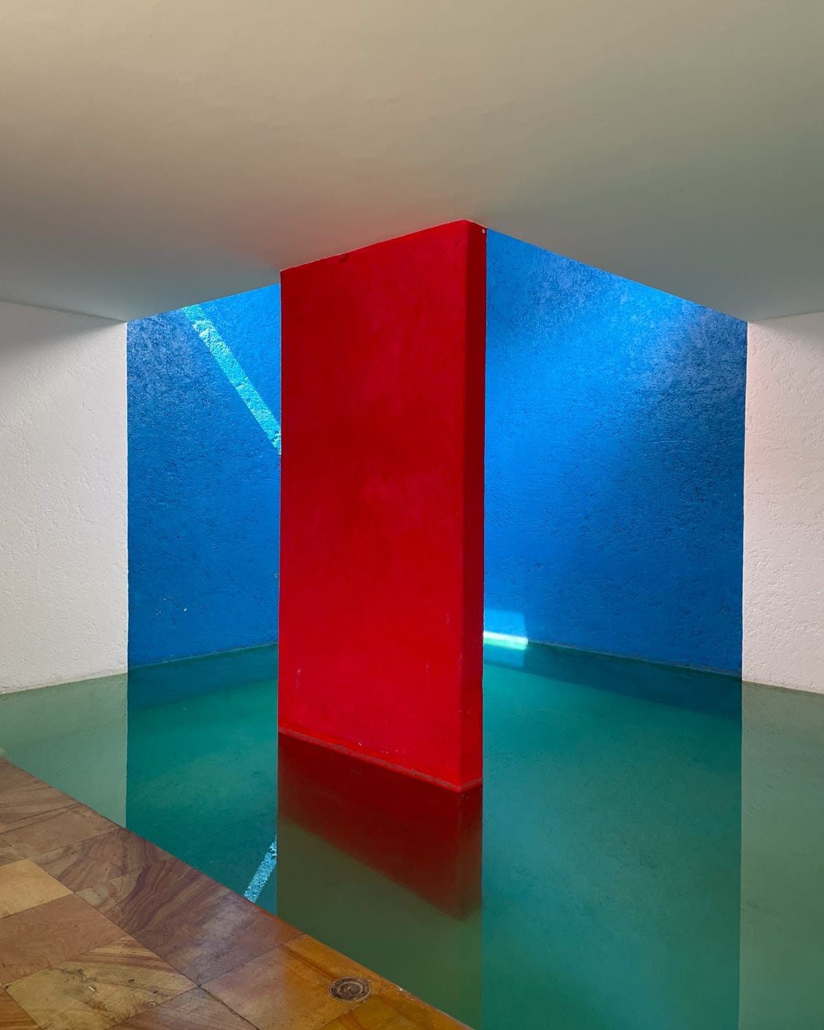 Bold geometric interior at Casa Gilardi in Mexico City, featuring red and blue walls with pool water reflections.