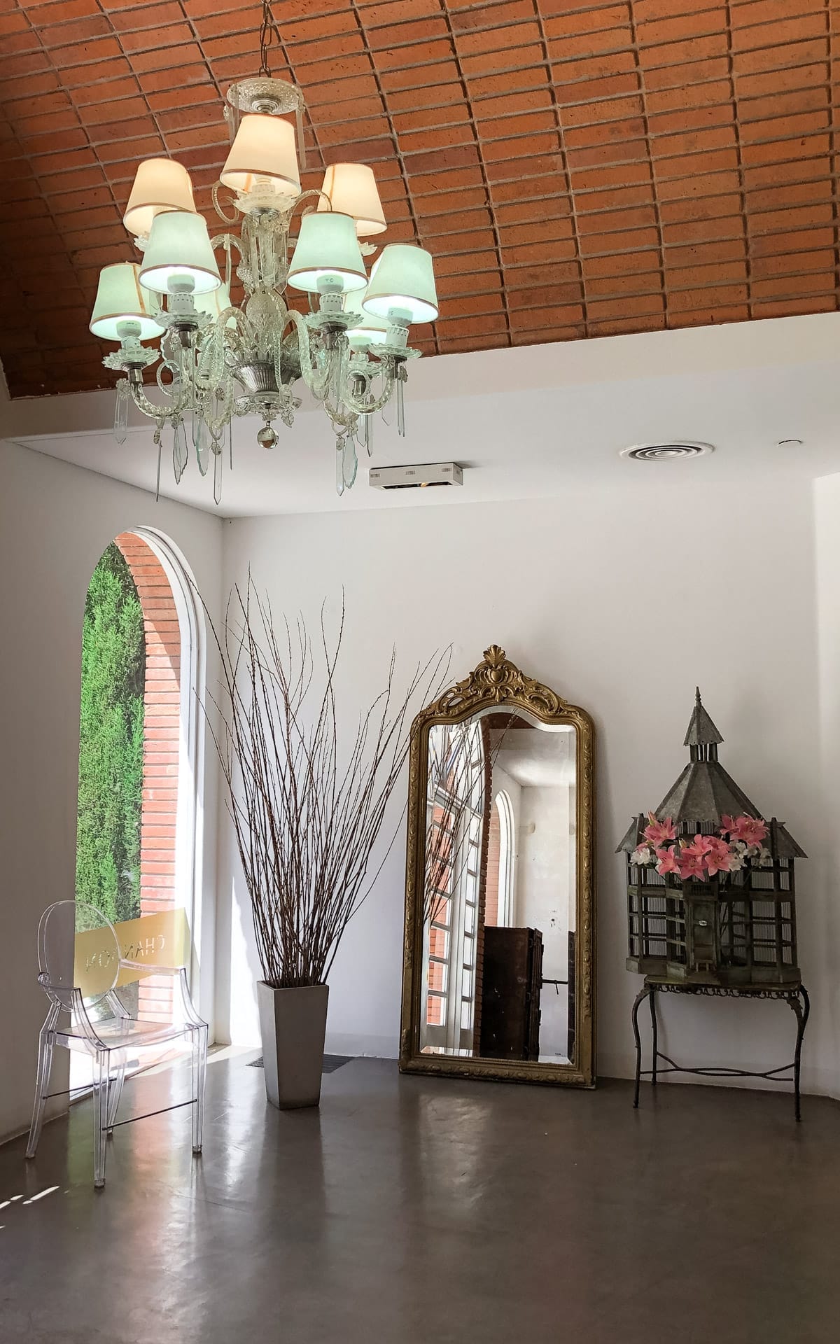Elegant corner at Chandon Winery featuring a chandelier, gold-framed mirror, ghost chair, and decorative birdcage.
