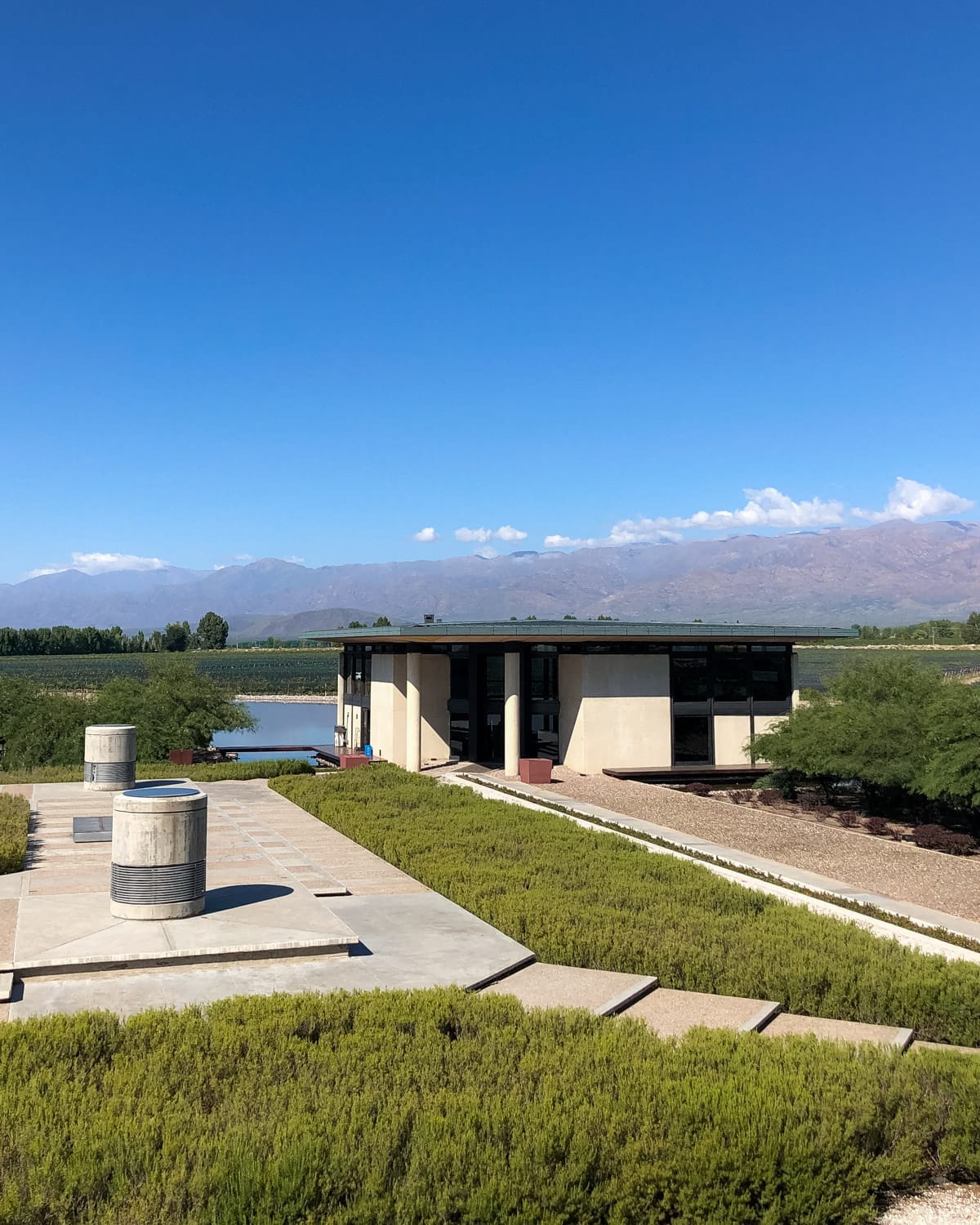 The modern Bodega Alfa Crux winery surrounded by vineyards and geometric landscaping, with Andes mountains rising in the background.