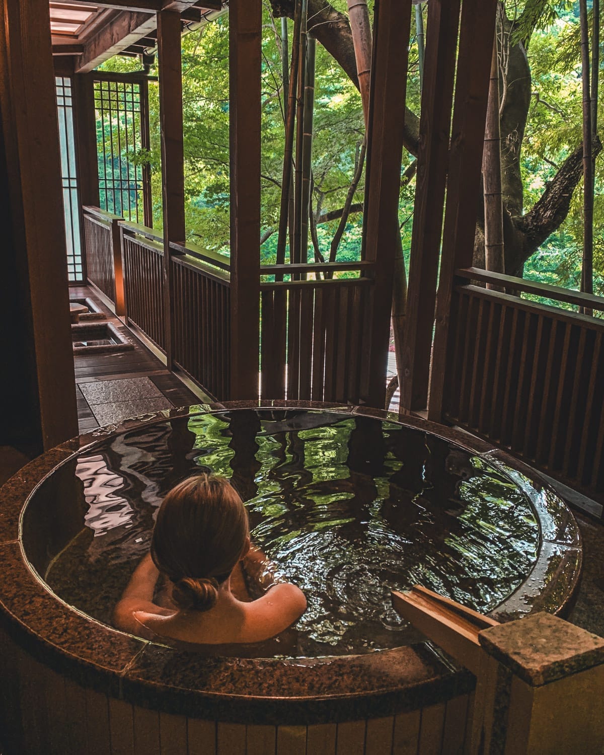 Cec soaking in a private round onsen on a balcony surrounded by bamboo and lush trees at a traditional ryokan.