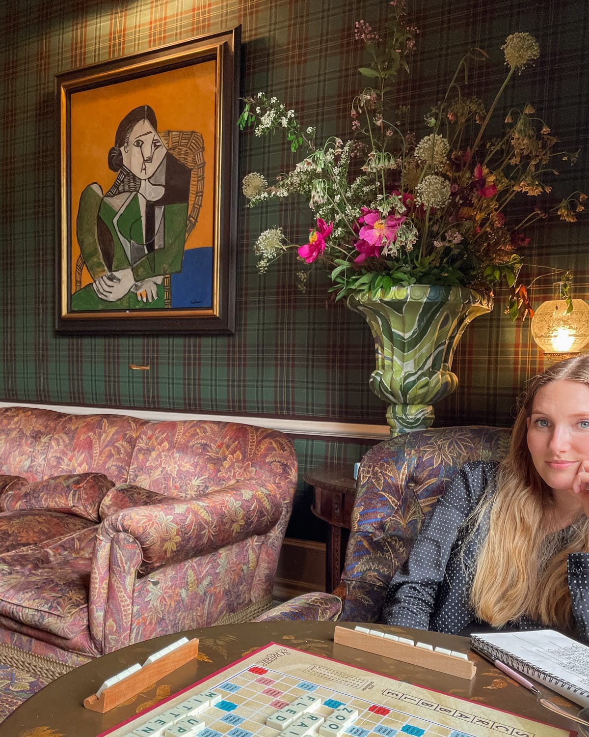 Cec playing Scrabble beneath a Picasso painting at The Fife Arms in Scotland, surrounded by floral decor.