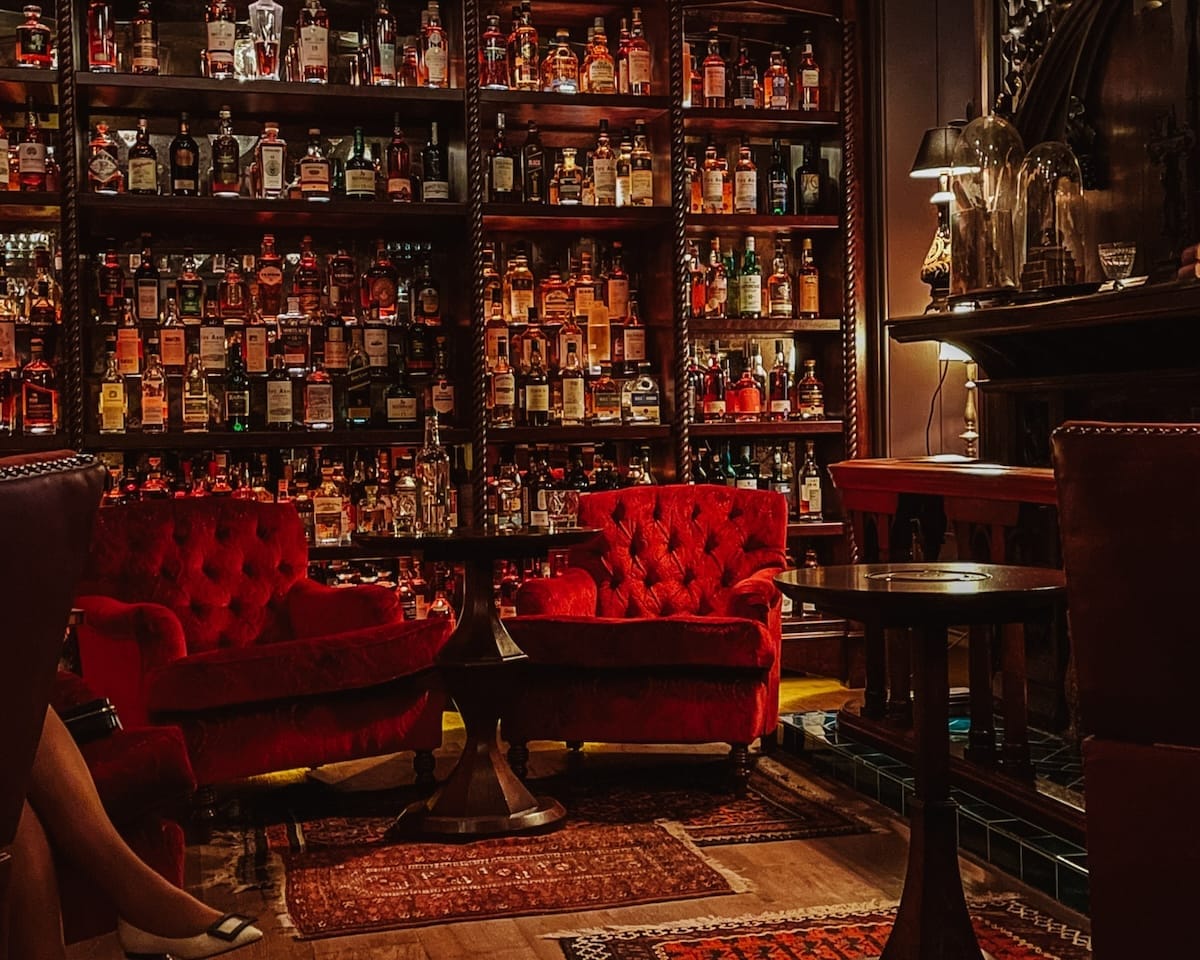 Dimly lit whisky bar with red velvet chairs, dark wood shelves, and hundreds of whisky bottles lining the back wall at The Fife Arms in the Scottish Highlands.