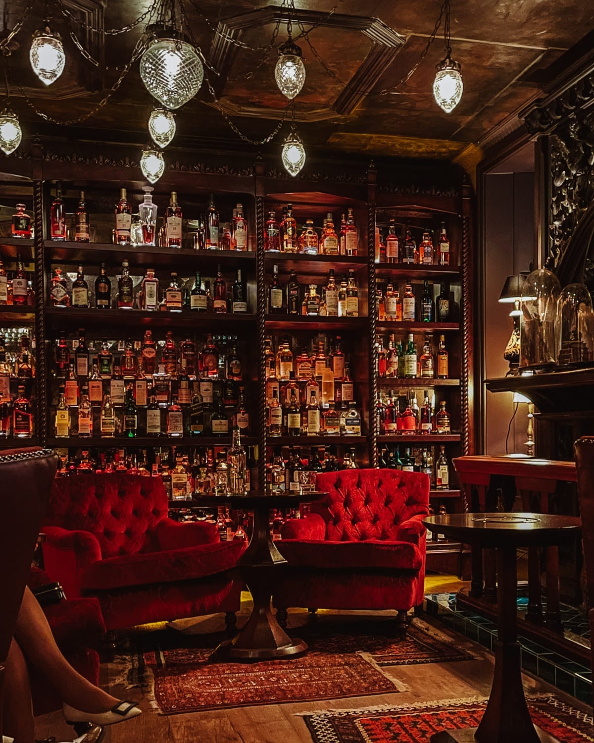 A dimly lit whisky bar with red velvet chairs and shelves full of spirits in vintage-style decor in the Scottish Highlands.