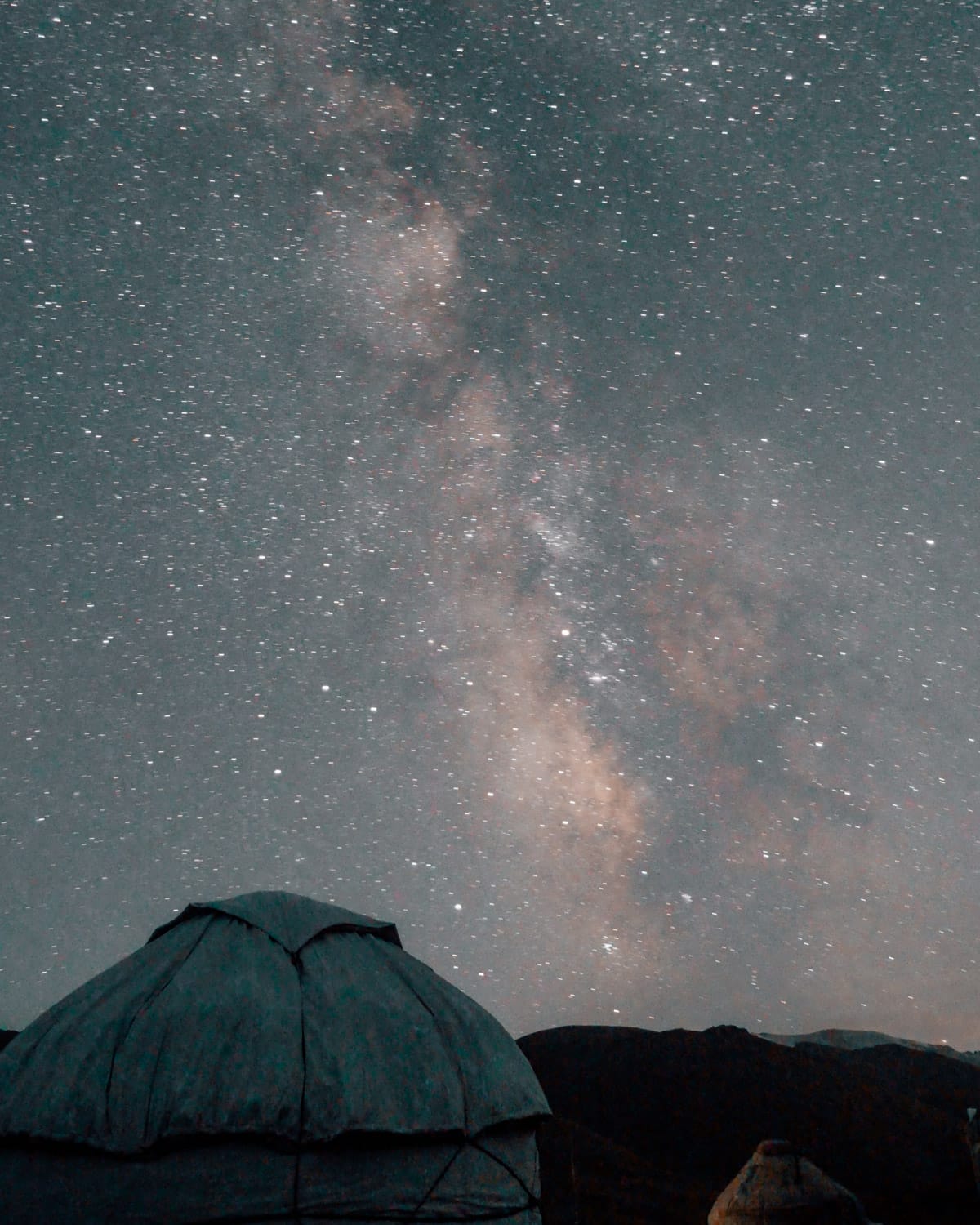 Milky Way shines brightly above yurts under the clear night sky in Kyrgyzstan’s remote alpine landscapes.