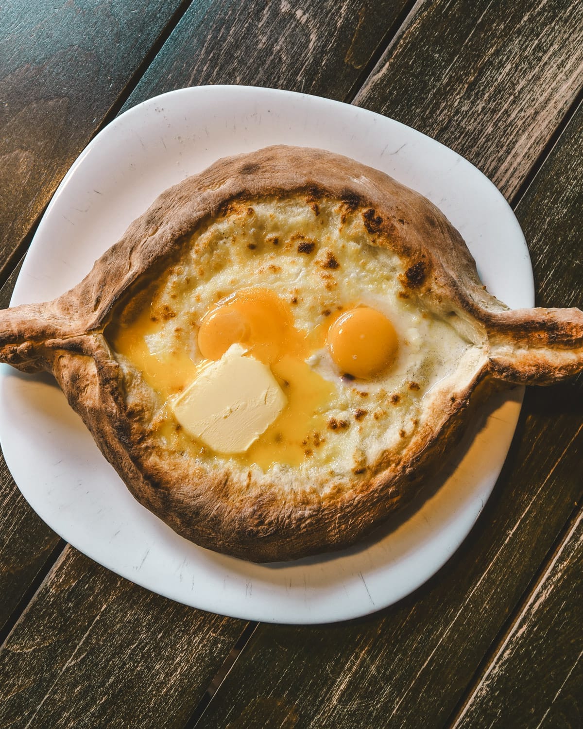 Close-up of khachapuri, Georgian cheese bread filled with melted cheese, egg yolks, and a slab of butter, served hot.