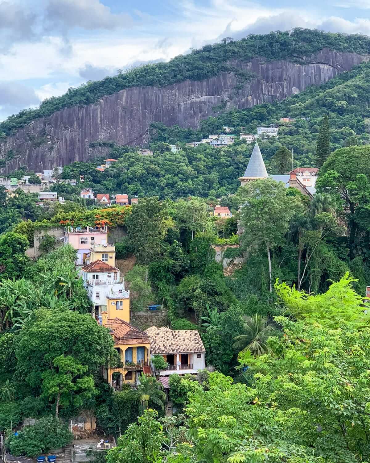 A lush green hillside in Santa Teresa with colourful colonial houses and a pointed church spire nestled in tropical forest.