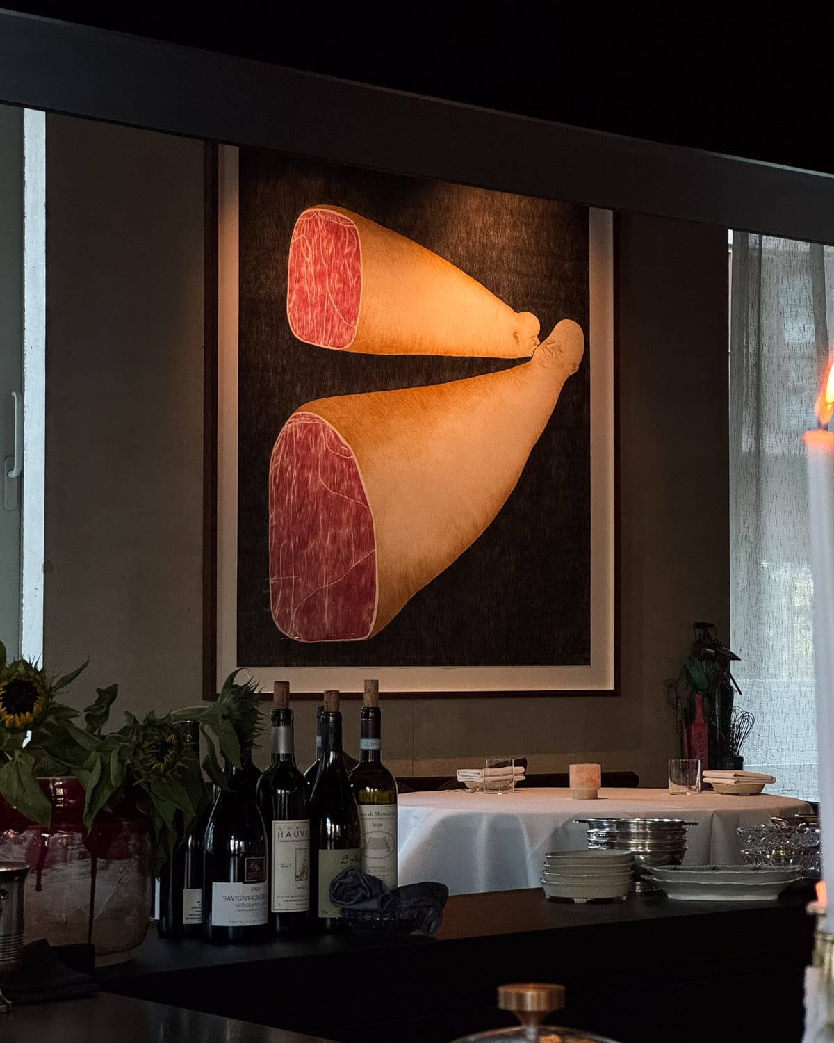 Inside Misera restaurant, a contemporary framed ham illustration hangs above a counter with wine bottles and minimalist table settings.