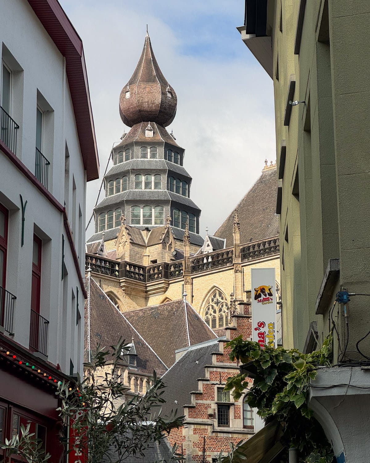 The unusual bulbous spire of a Gothic church peeks through narrow streets in Antwerp.