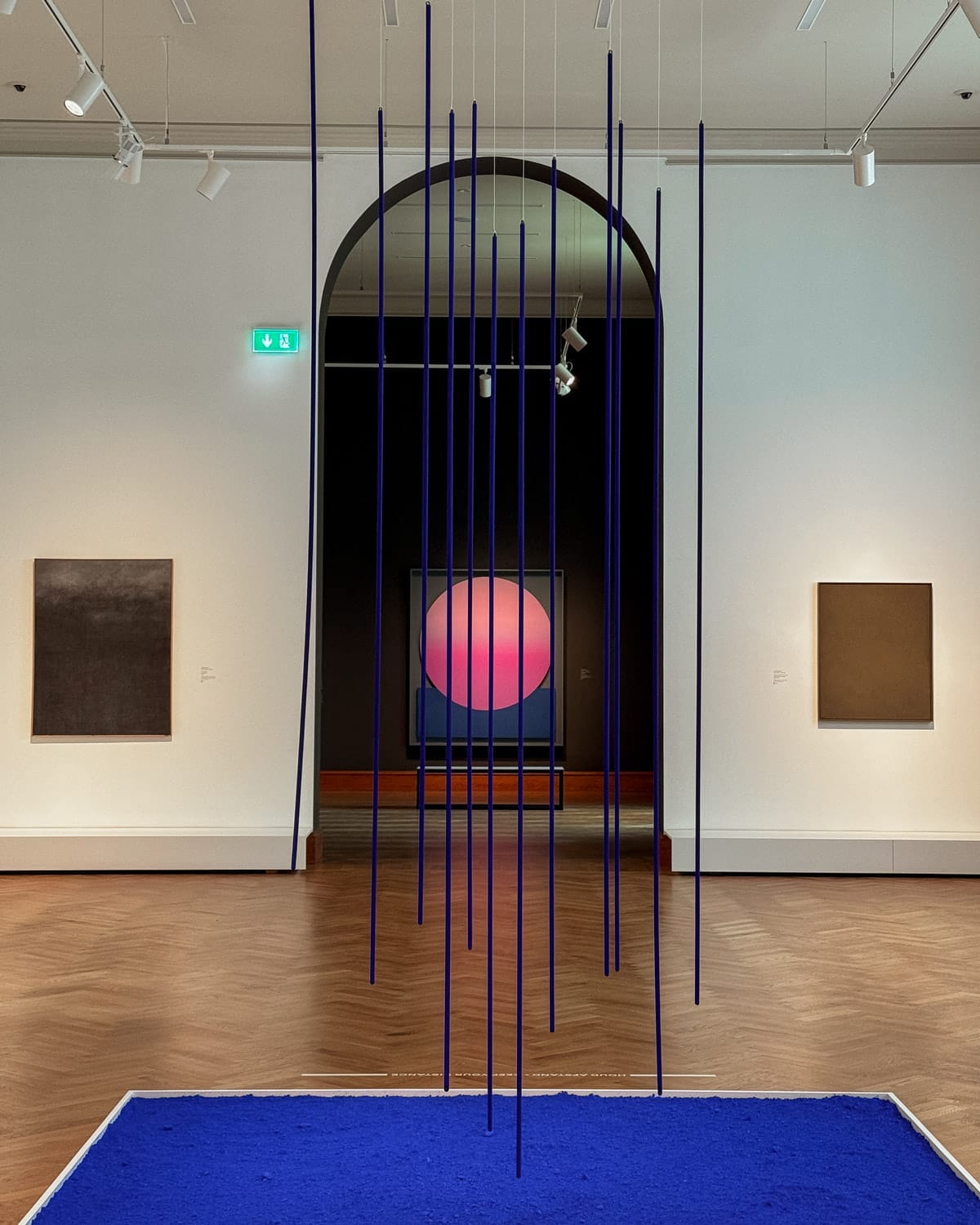 A contemporary art piece with vertical blue rods suspended over cobalt pigment, with a glowing gradient circle artwork by Jef Verheyen in the background at KMSKA.