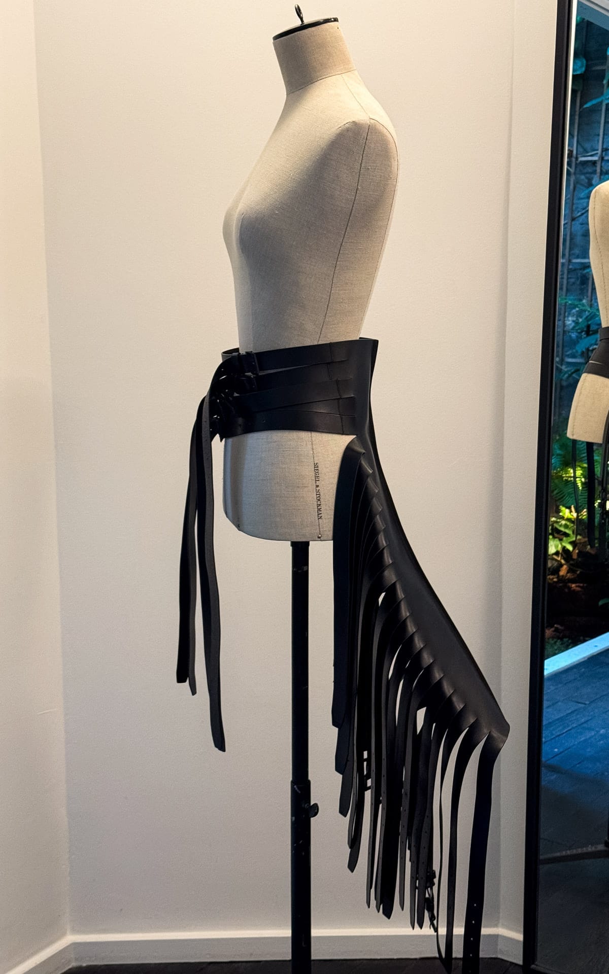 A mannequin displays an edgy black leather belt with long, structured fringe by Anne Demeulemeester.