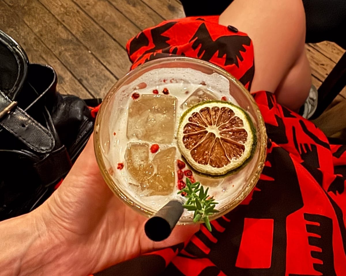 Cec holds a gin cocktail with ice, a dried lime slice, pink peppercorns, and herbs at Jones & Co. in Antwerp.