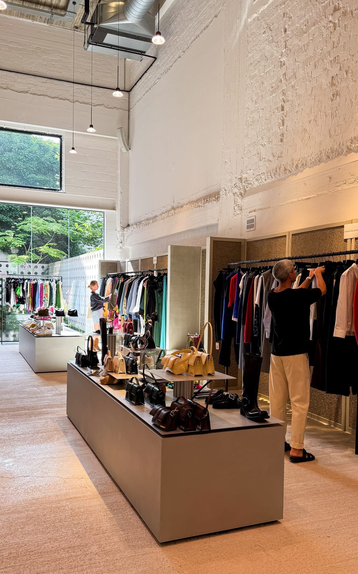 Inside the contemporary Renaissance boutique with high ceilings, designer handbags and clothes neatly displayed while shoppers browse racks.