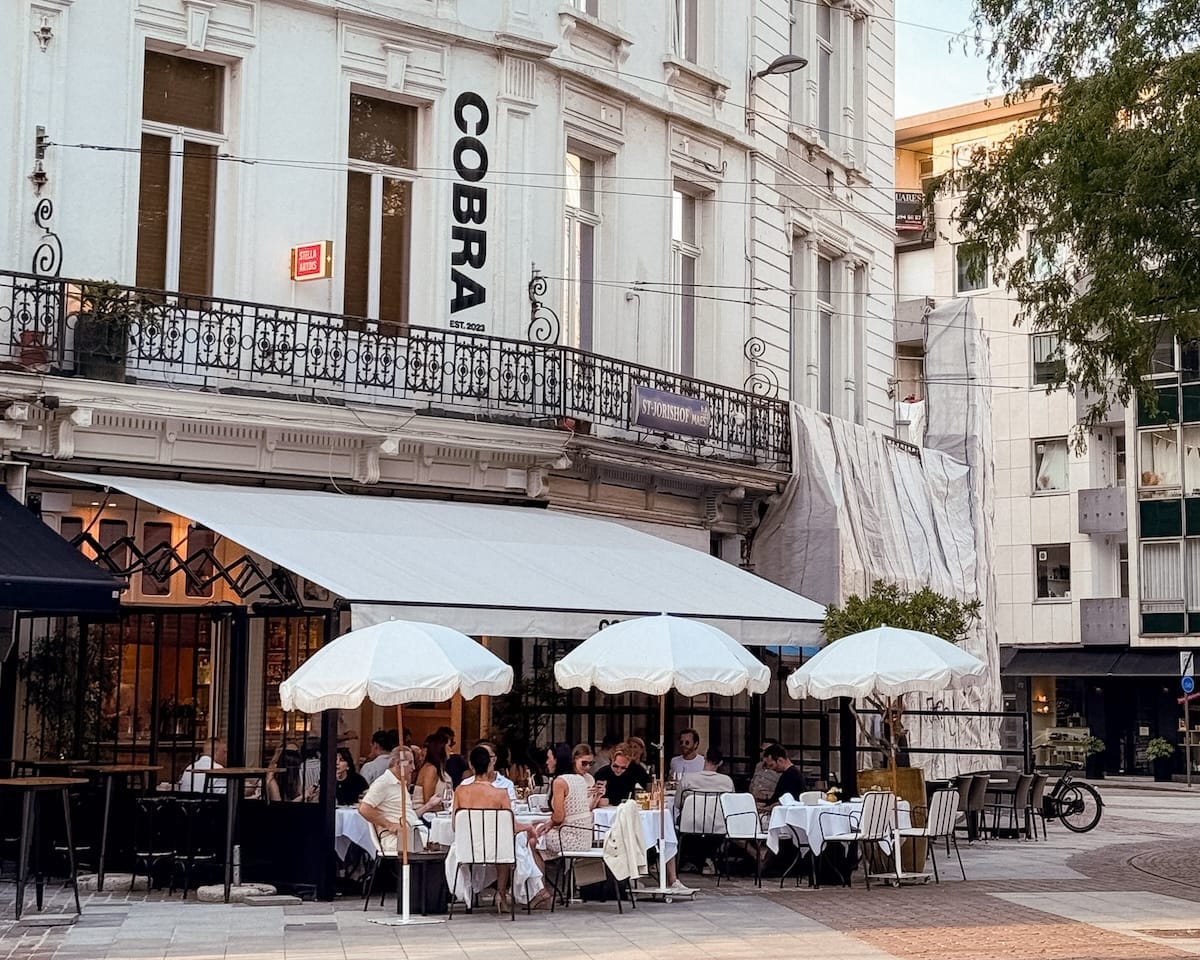 Diners sit under white umbrellas outside Cobra restaurant, housed in a classic white building.