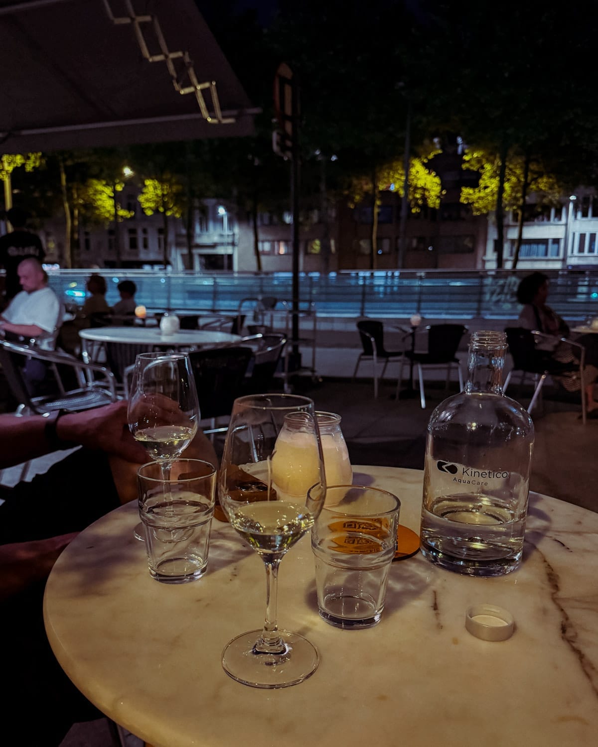 Outdoor patio of Osaka bar with a marble table set with wine glasses and a candle framed by evening streetlights.