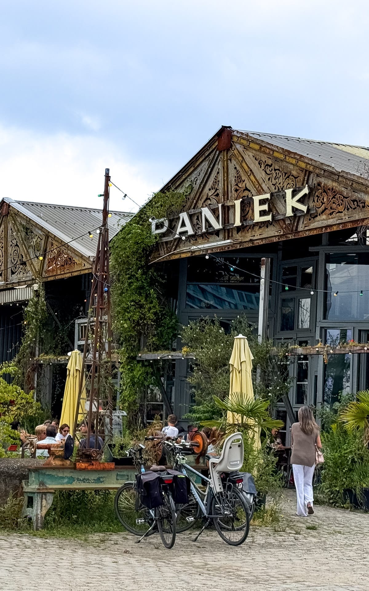 Rustic exterior of Paniek bar with ornate metal details, ivy-covered walls, patio seating, and parked bikes.