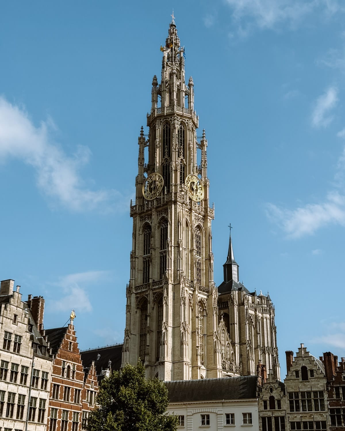 The soaring Gothic spire of the Cathedral of Our Lady rises above Antwerp, with twin clock faces and detailed stonework.