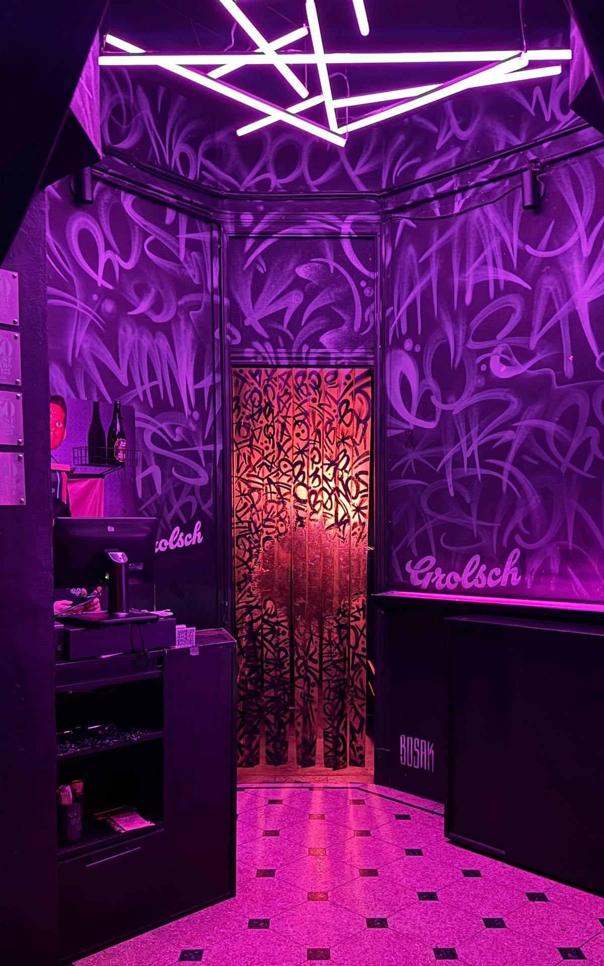 Neon-lit entrance of Tres Monos with purple graffiti walls and geometric ceiling lights glowing above.