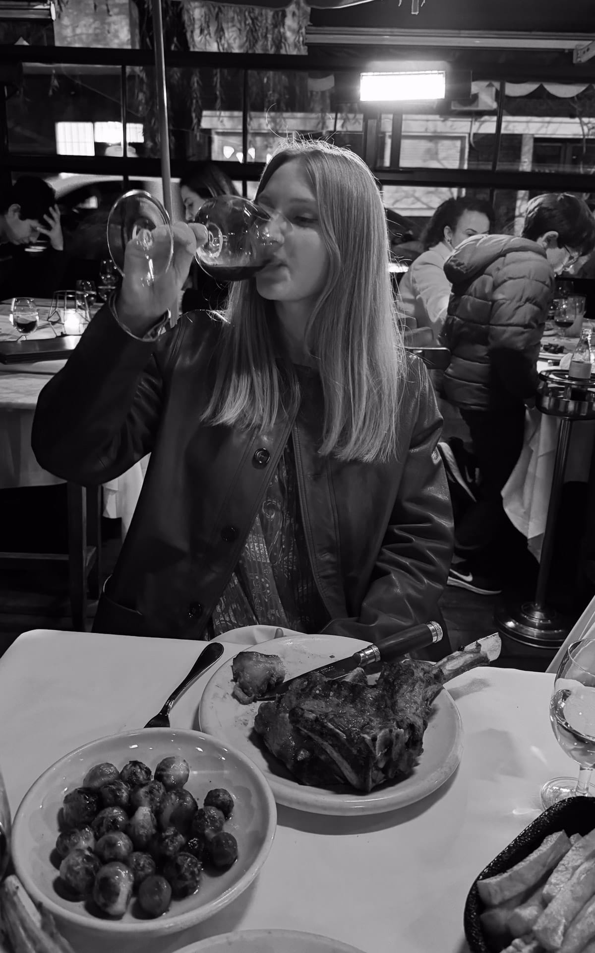 Cec sipping red wine at Don Julio parrilla with a bone-in ribeye steak and brussel sprouts.