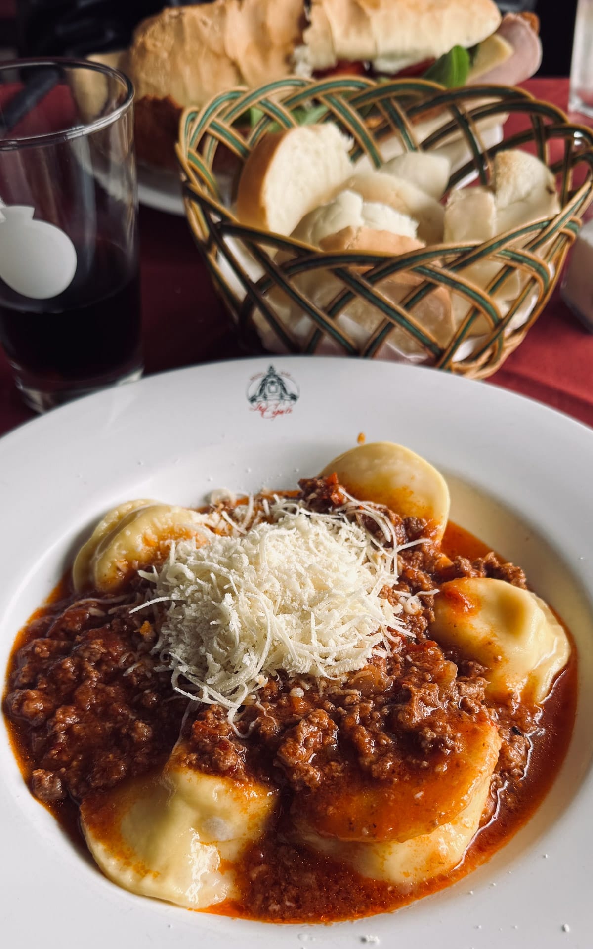 Plate of sorrentinos topped with Bolognese sauce and parmesan, served with bread basket and red wine at Los Dos Hermanos in Buenos Aires.