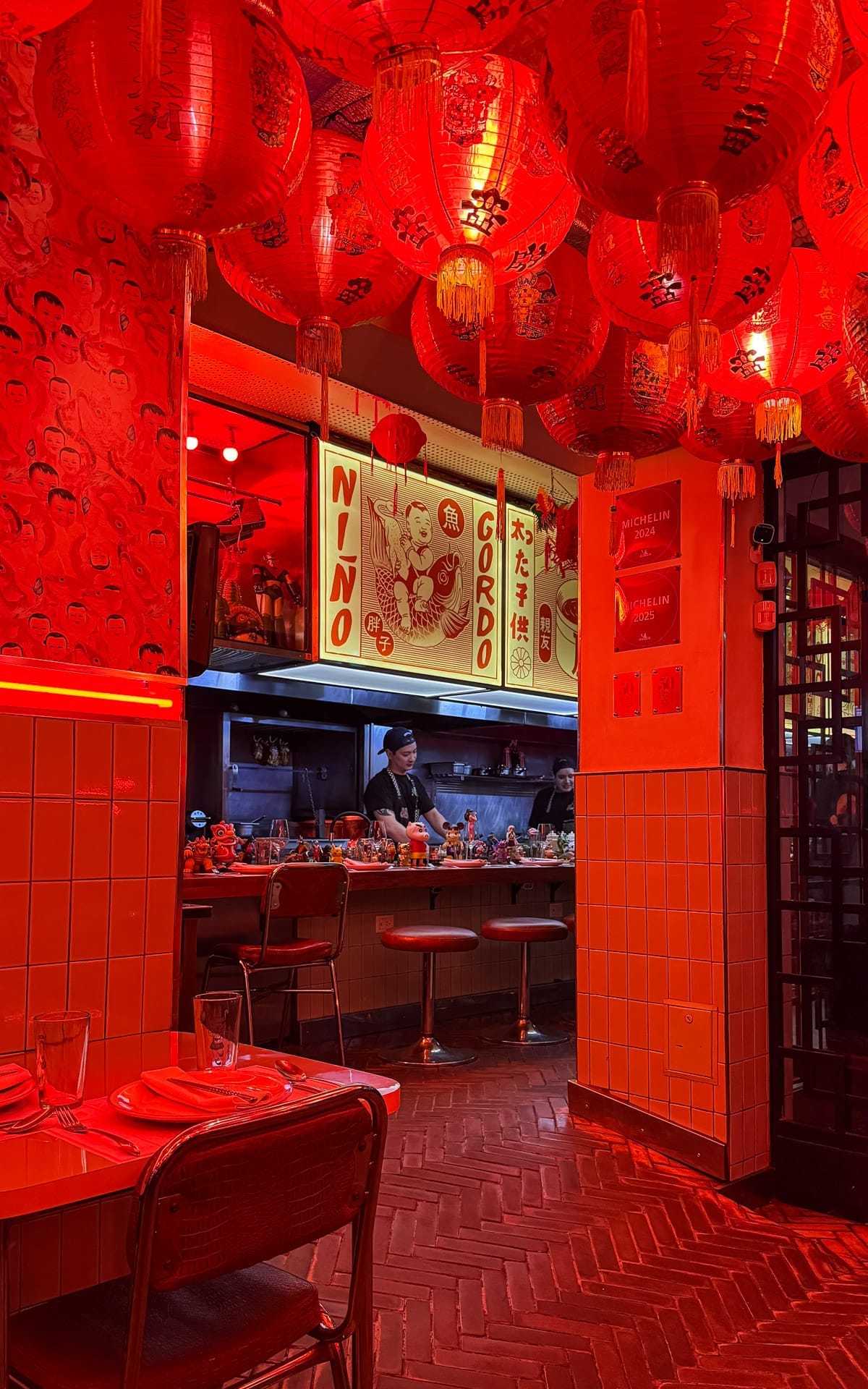 Inside Niño Gordo, a buzzing Buenos Aires restaurant glowing red with lanterns, open kitchen views, and eclectic decor