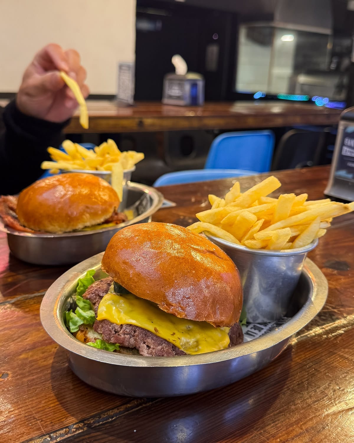 Classic cheeseburger with fries served in metal trays on a wooden table at Perez H in Palermo.
