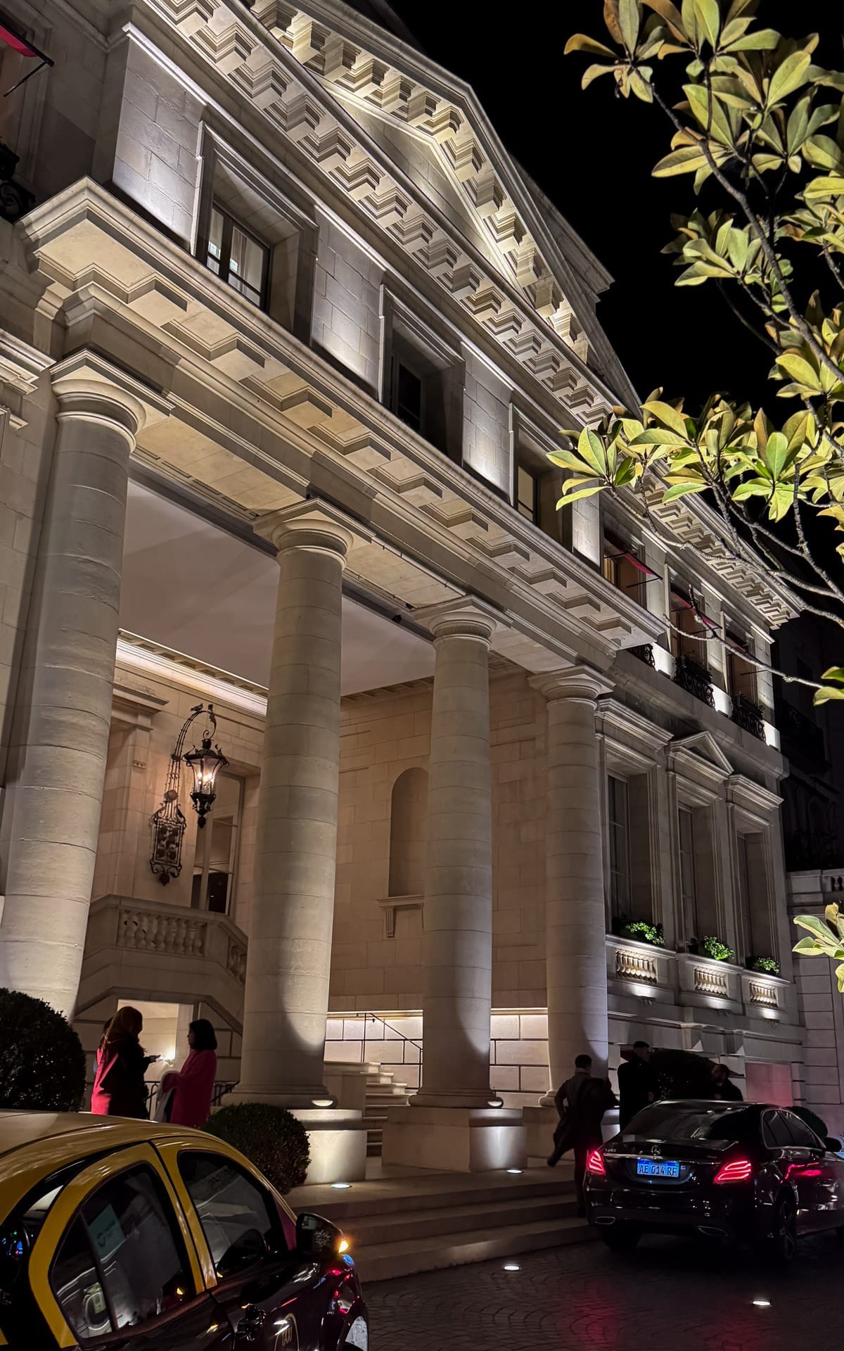 Night view of Palacio Duhau's elegant neoclassical hotel entrance, lit dramatically with columns and luxury cars outside.