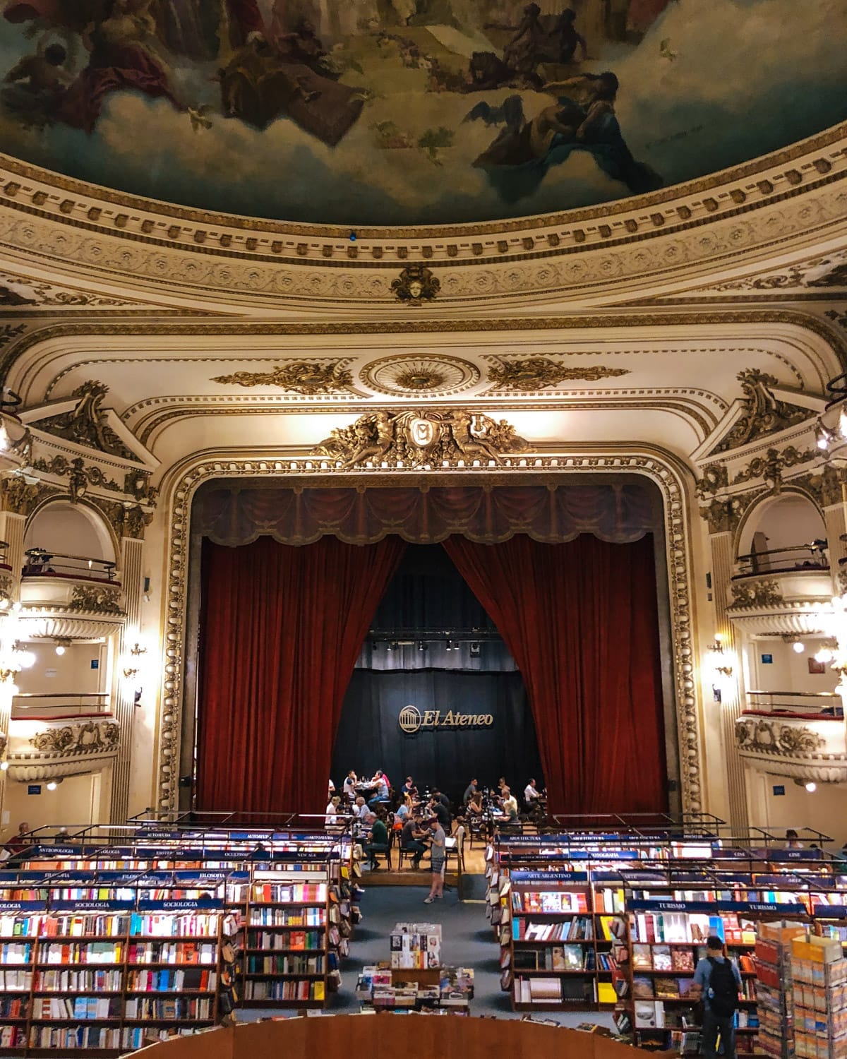 The grand interior of El Ateneo Grand Splendid, a former theater turned bookstore, with shelves of books filling the stage and ornate frescoes overhead.