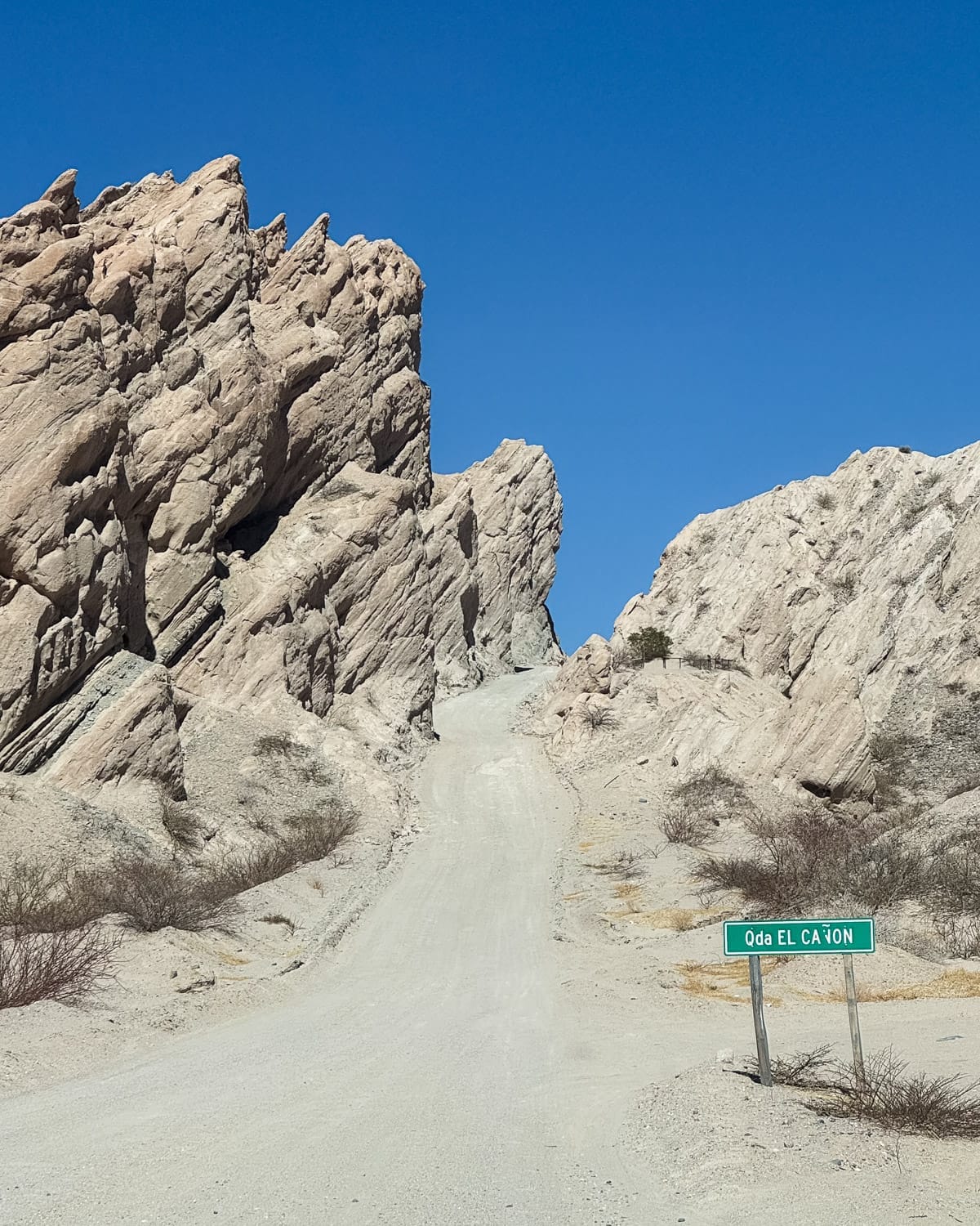 Narrow gravel road winding through dramatic rock formations under a clear blue sky in Quebrada de las Flechas. 