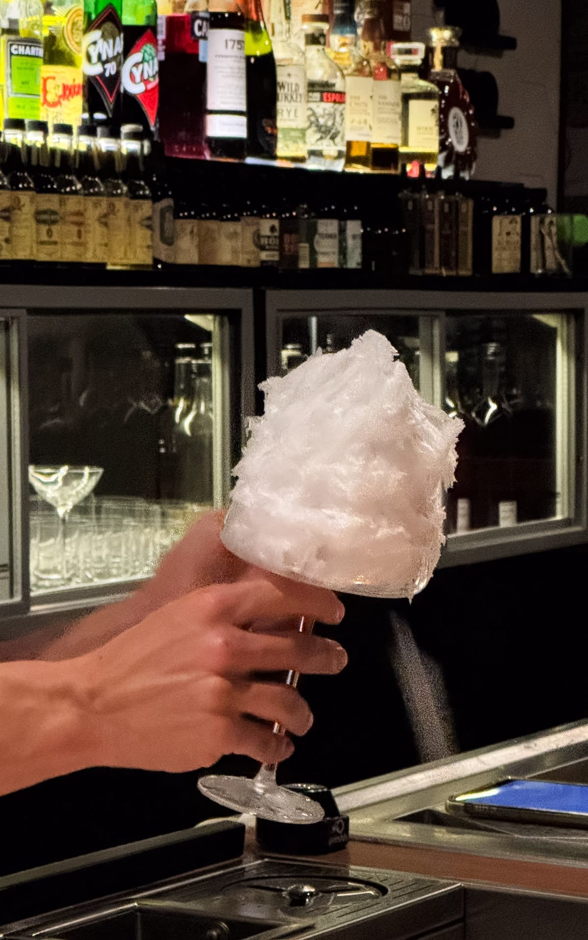 Bartender holding a cocktail topped with fluffy cotton candy-looking ice at Tan Tan in São Paulo.