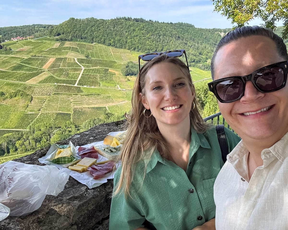 Cec and Ari enjoying a picnic viewpoint above Château-Chalon with vineyards in the background.
