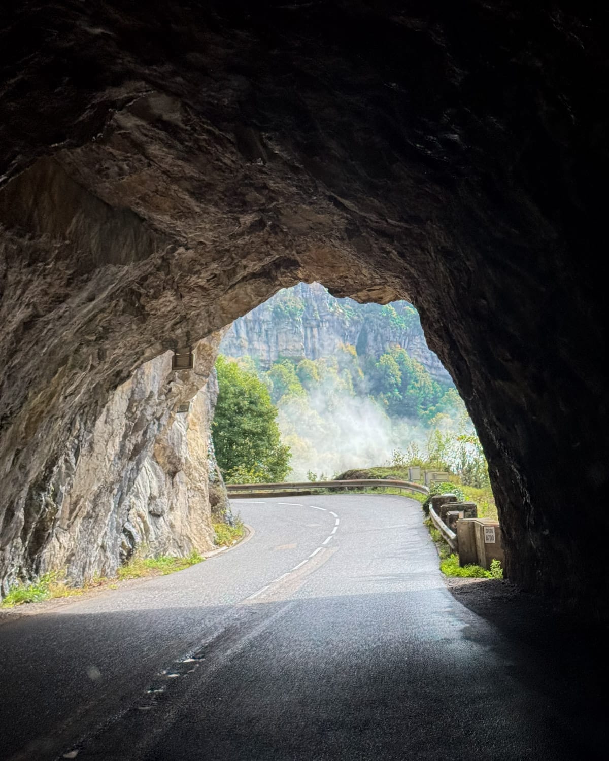Driving through a rock tunnel on a scenic mountain road in the Haut-Jura Regional Natural Park.