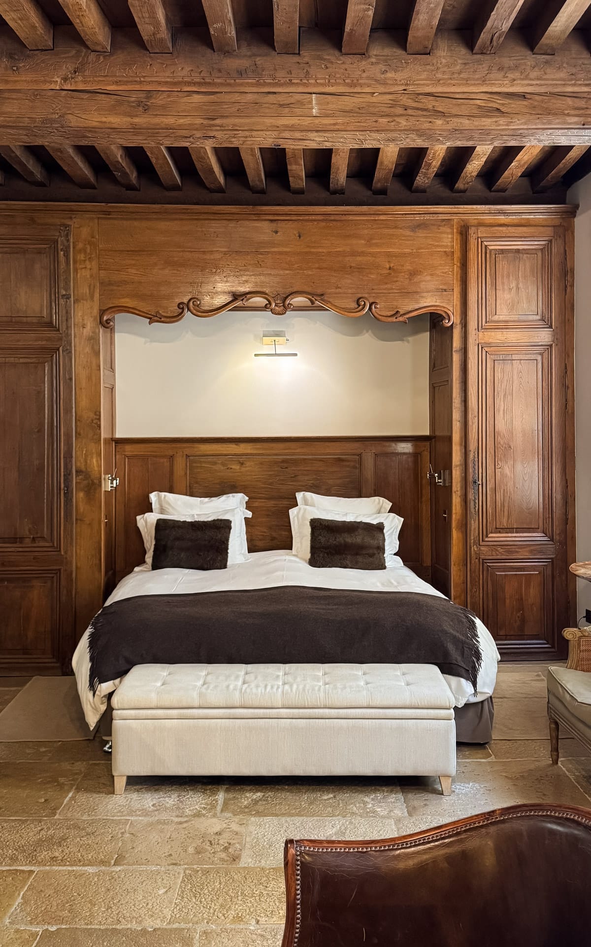 Rustic guest room at Le Clos Sainte Marguerite in Beaune with exposed wooden beams, stone floors, and carved wood details.