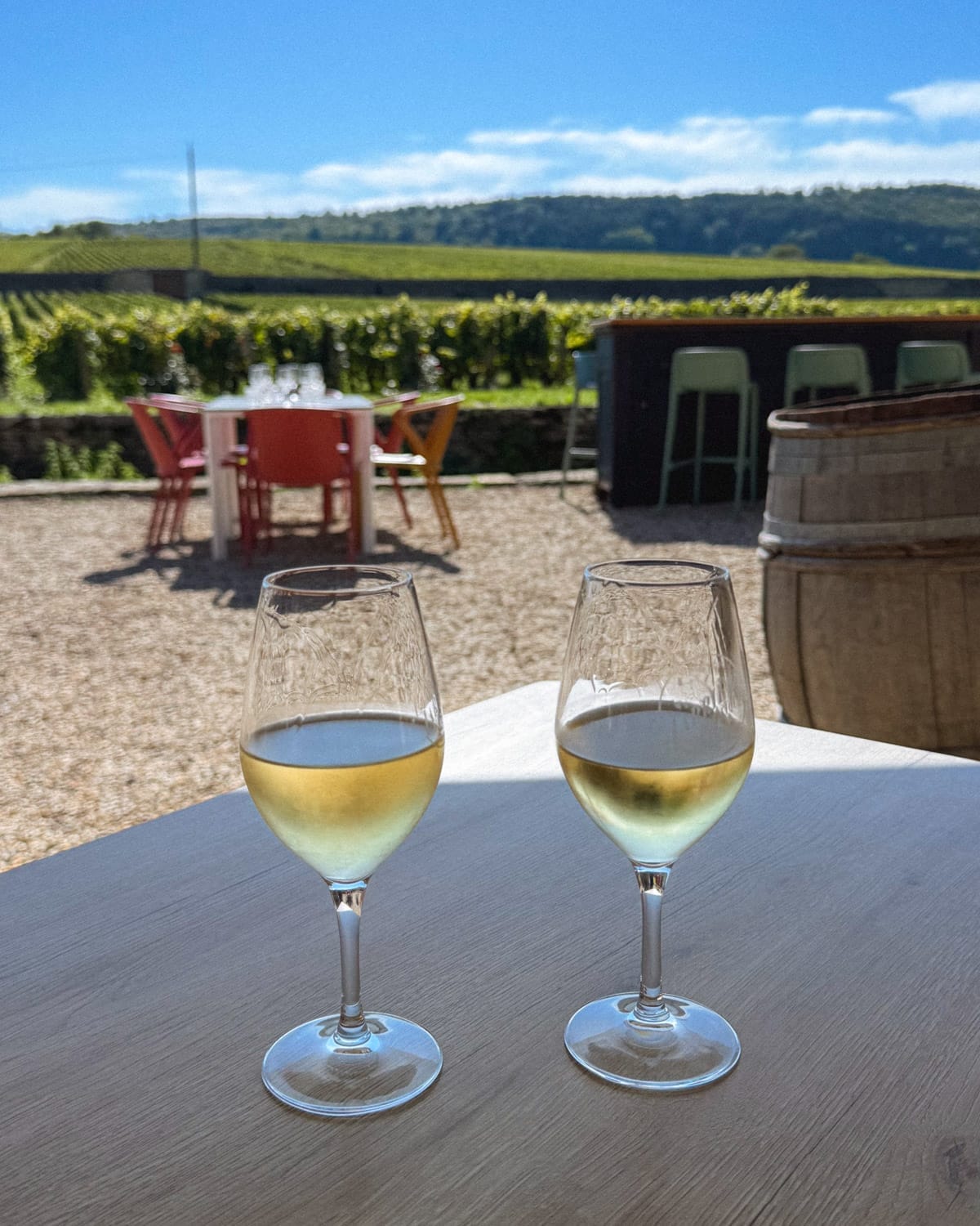 Two glasses of white Burgundy wine on an outdoor table at Clos du Moulin aux Moines overlooking vineyards