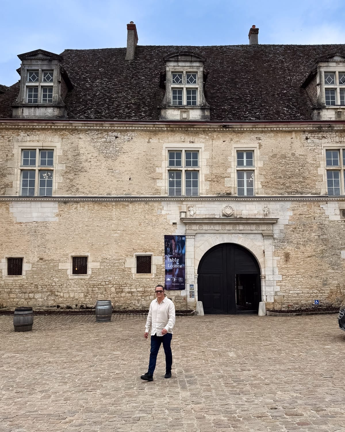 Ari standing in the stone courtyard of Château du Clos de Vougeot with its central arched entrance.