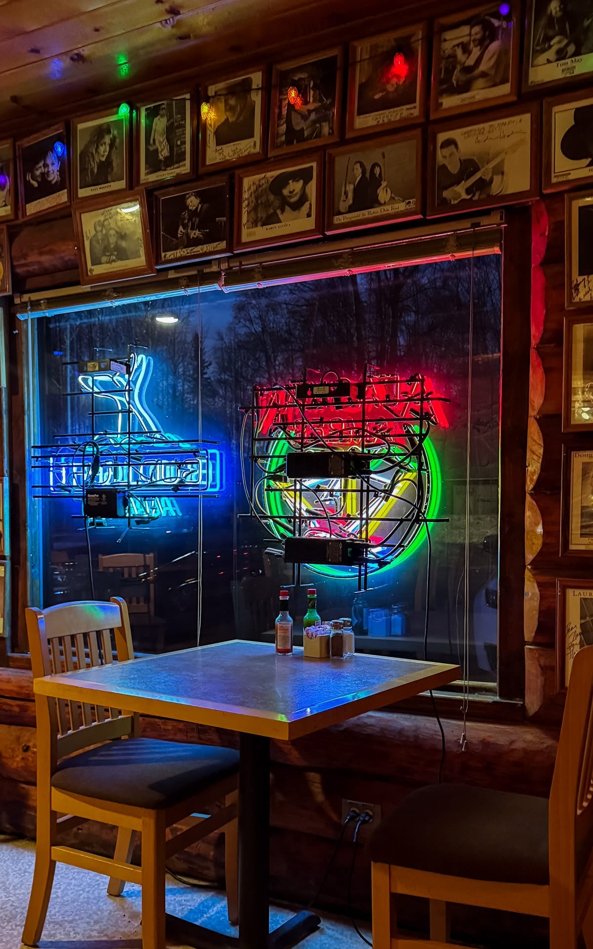 Neon beer signs glowing in a rustic log cabin restaurant at Latitude 62 in Talkeetna, with framed musician portraits lining the walls.