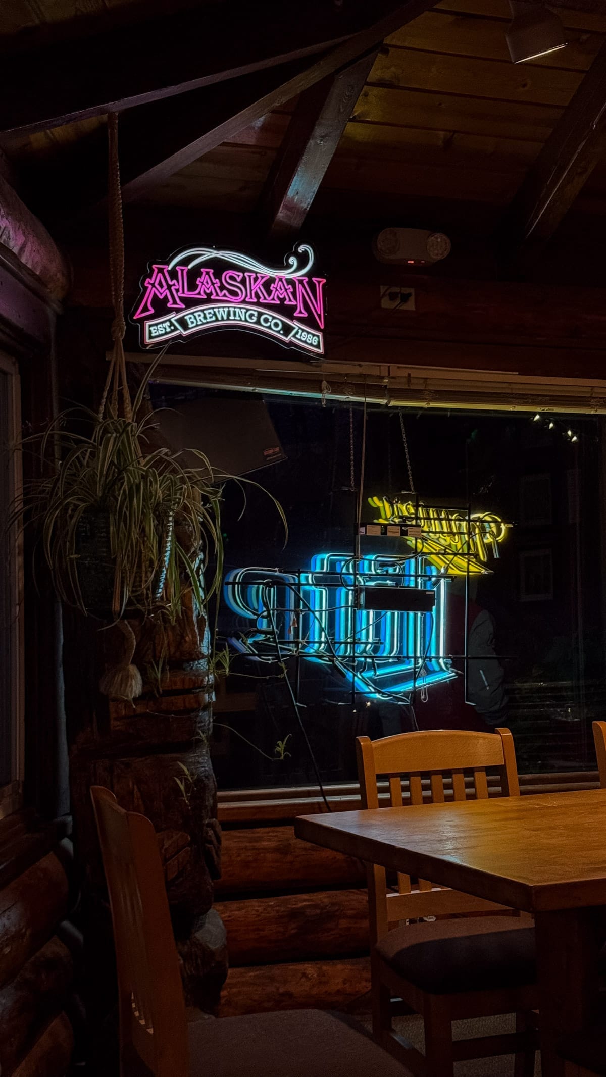 Pink Alaskan Brewing Co neon sign glowing inside a dimly lit log cabin-style restaurant.