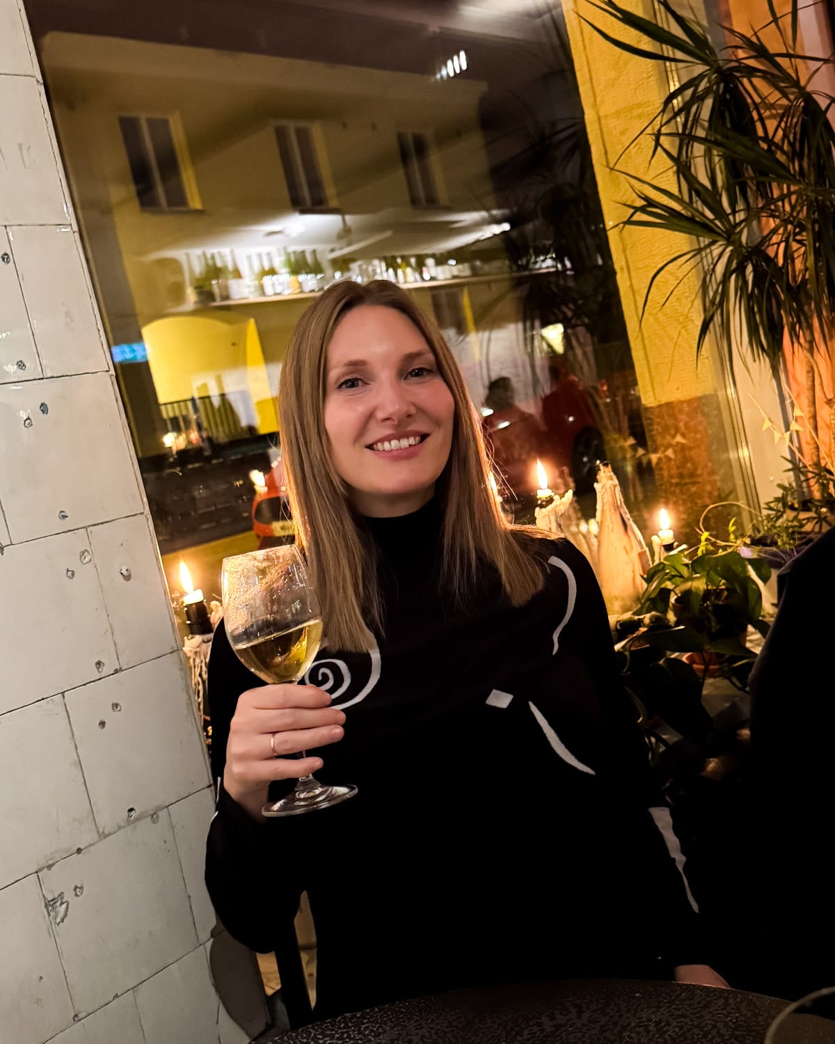 Cec holding a glass of white wine at candlelit Plein restaurant at night