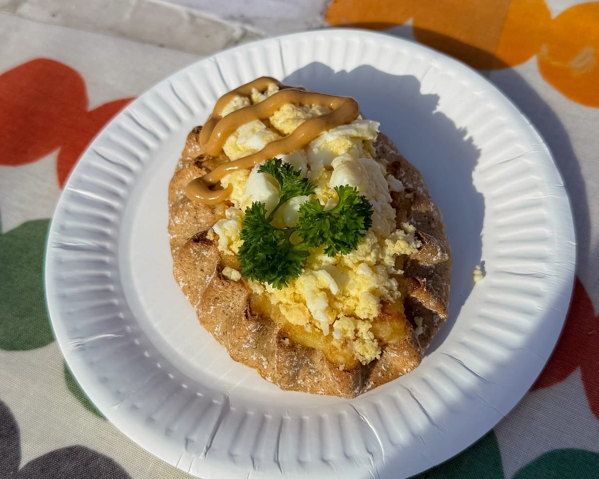 Karjalanpiirakka topped with egg butter and mustard on a paper plate at Helsinki Market Square.