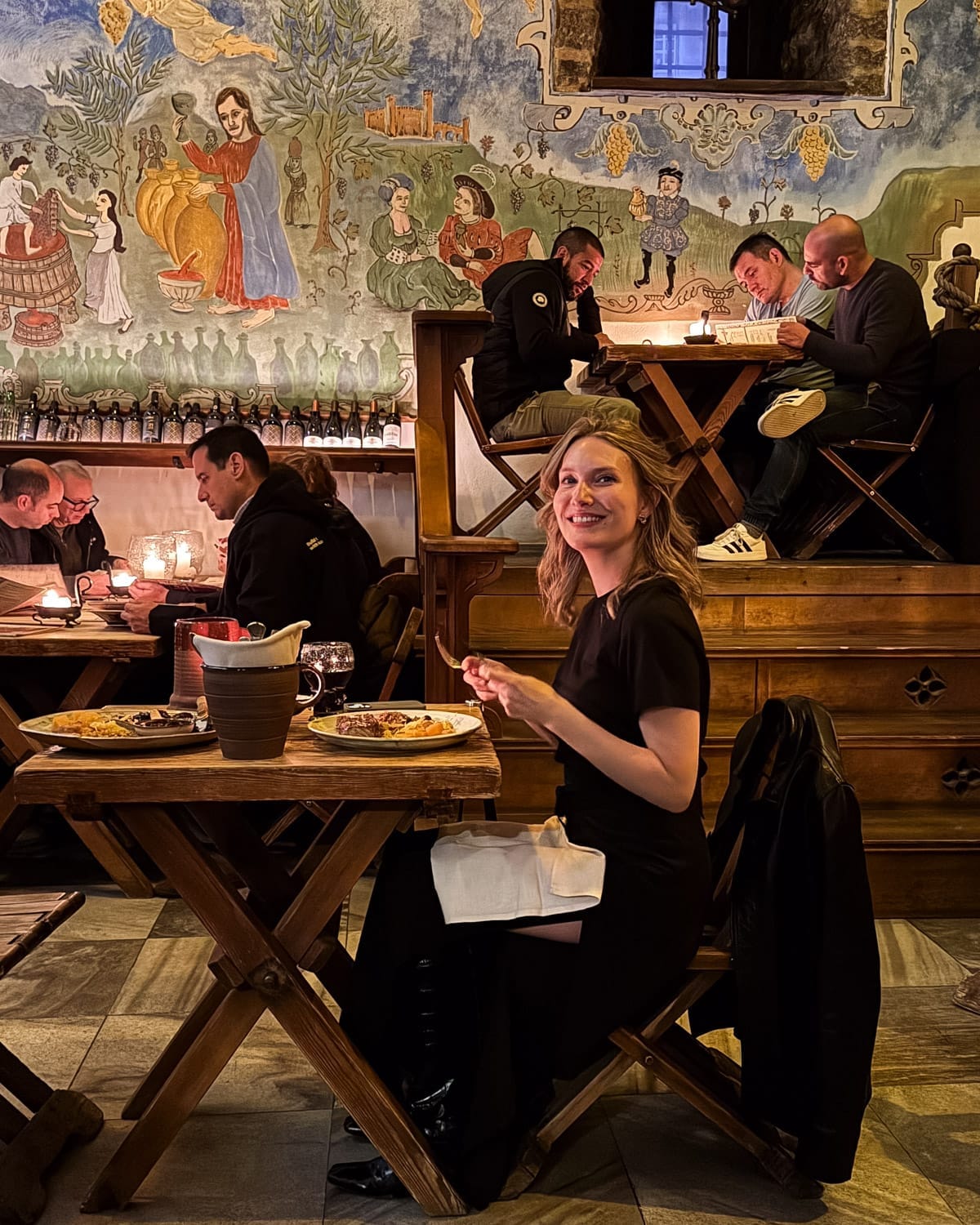 Cec dining inside medieval-style Olde Hansa restaurant in Tallinn with painted murals and candlelit tables.