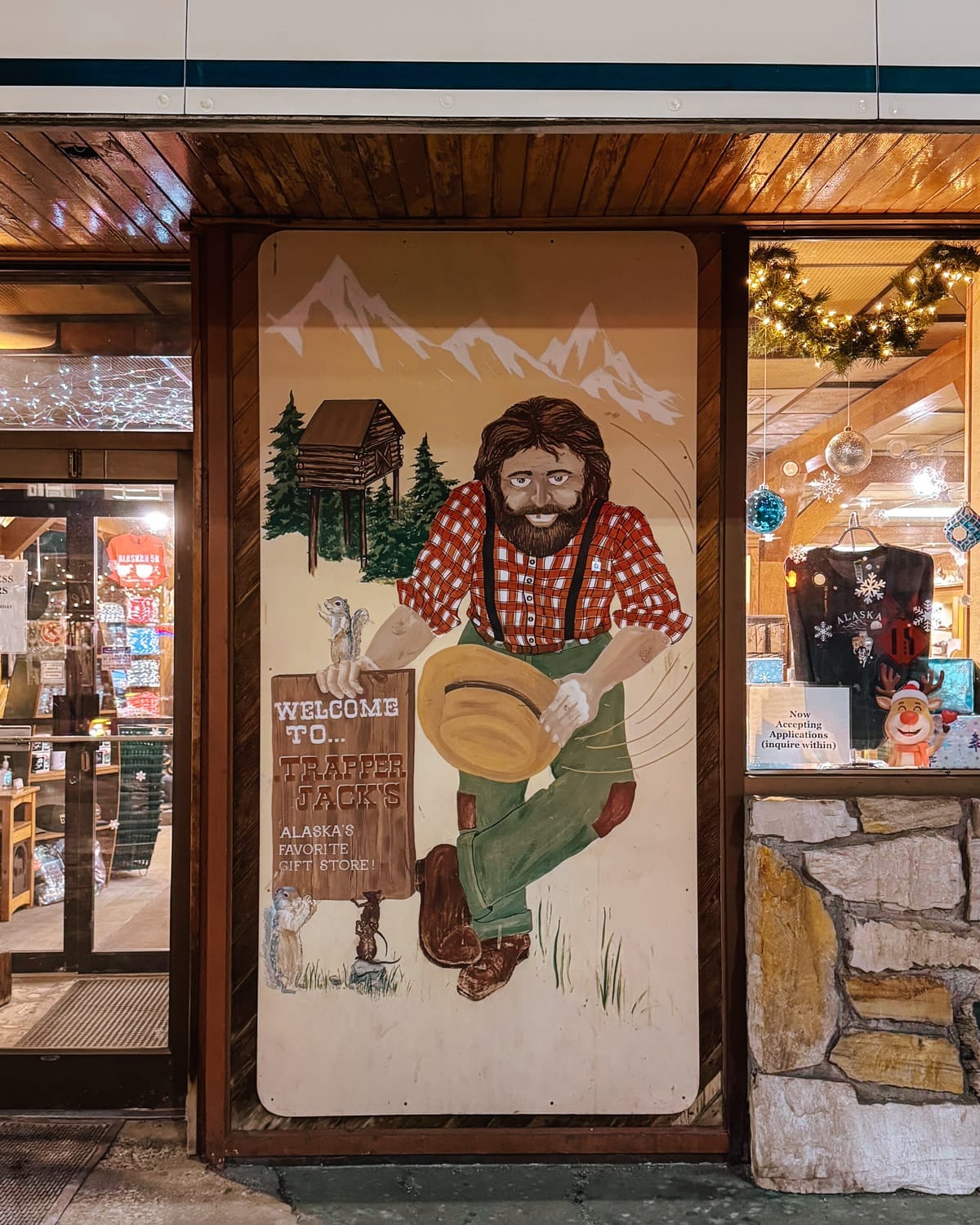 Mural outside Trapper Jack’s gift store in Anchorage featuring a bearded frontiersman holding a hat, with mountains, a cabin and wildlife illustrated behind him.