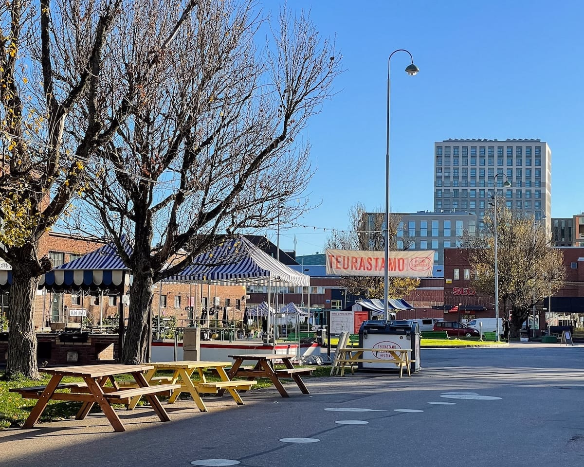Open courtyard at Teurastamo cultural hub in Helsinki with picnic tables and striped market tents.