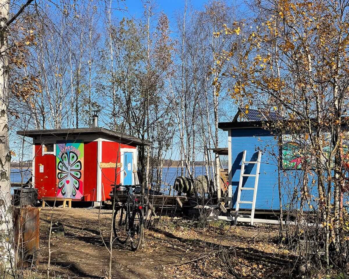 Colourful wooden sauna huts at Sompasauna by the waterfront in Helsinki, surrounded by autumn trees.