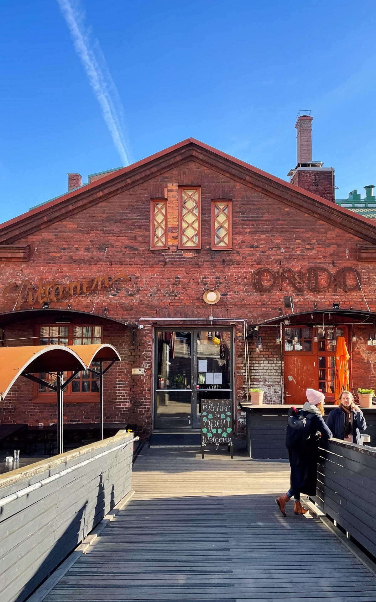 Siltanen, a red brick industrial building in Kallio with people standing outside on a wooden walkway.