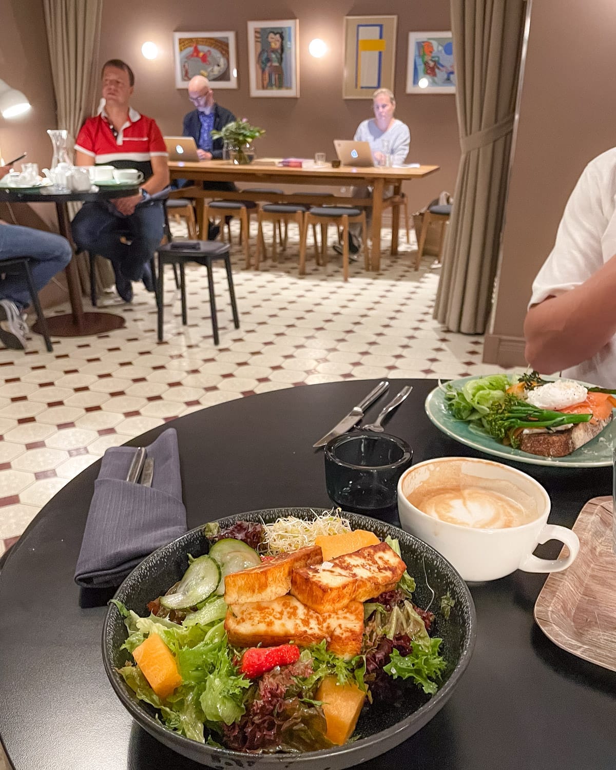 Halloumi salad and latte on a cafe table in Helsinki, with locals working on laptops in the art-filled St. George Bakery.
