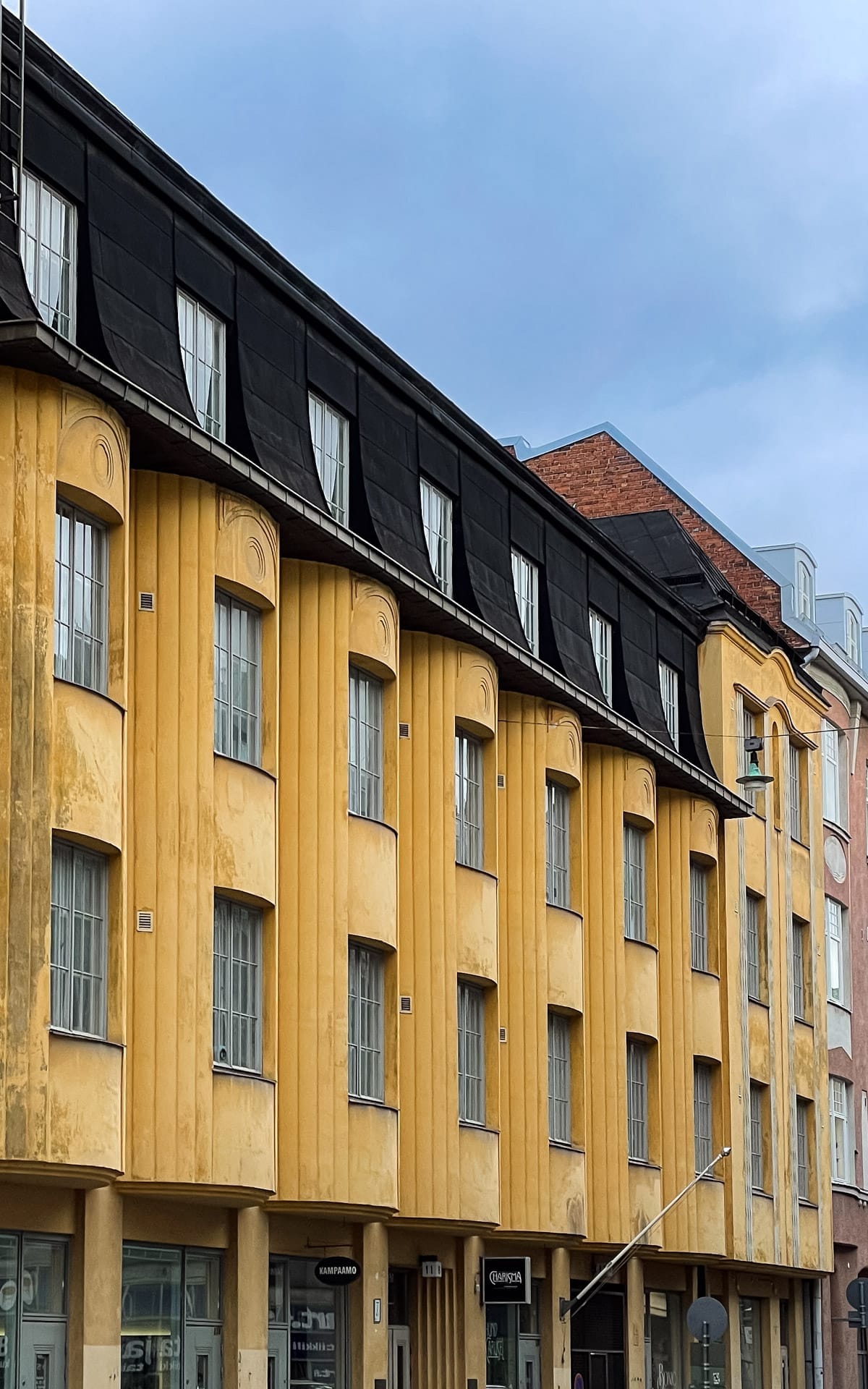 Row of mustard-yellow buildings with black mansard roofs along a quiet Helsinki street.