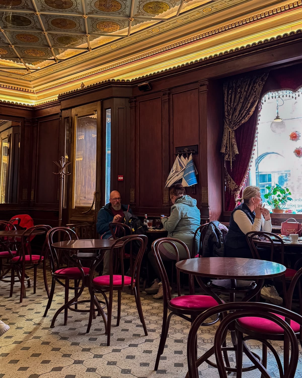 Interior of Estonia’s oldest cafe with ornate ceiling, dark wood panels and red velvet chairs.