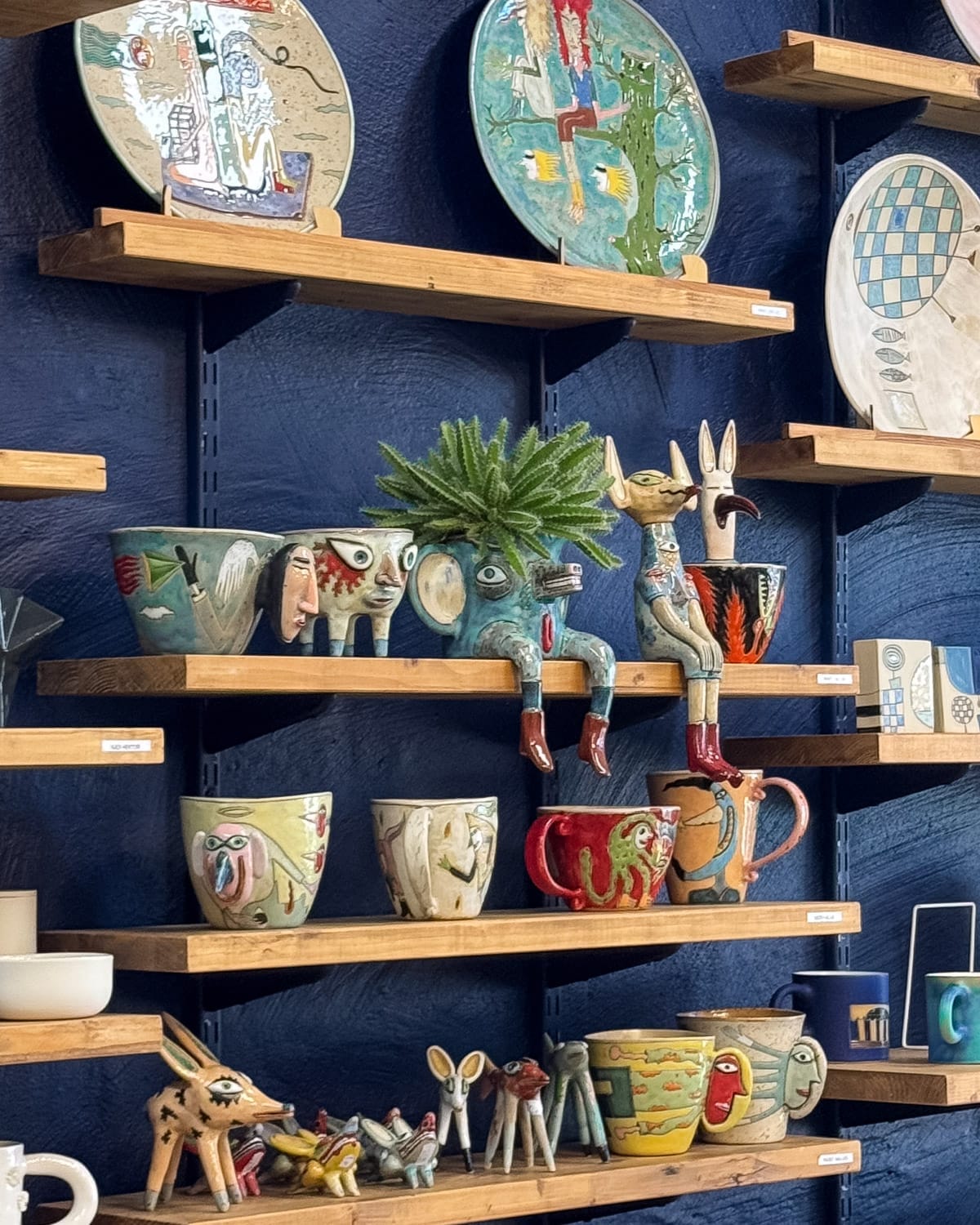 Handcrafted ceramic mugs and eclectic figurines displayed on wooden shelves at TEKE Keraamika.