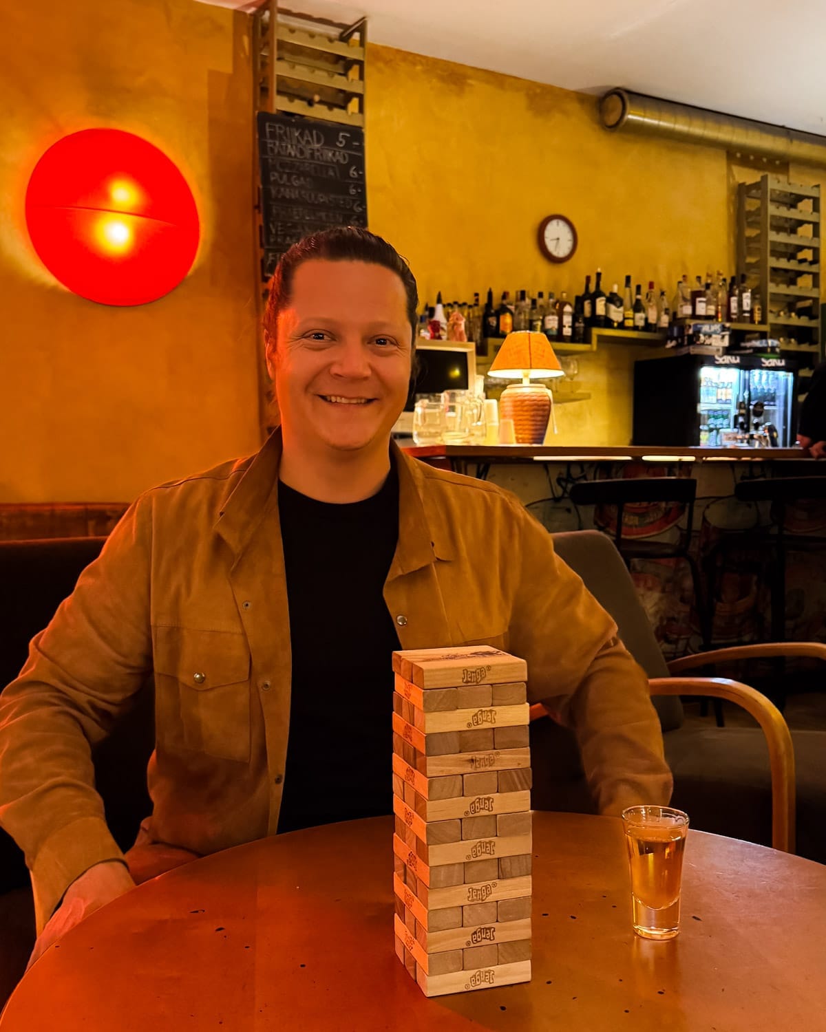 Ari playing Jenga at warmly lit NoKu bar with bottles lined behind the counter.