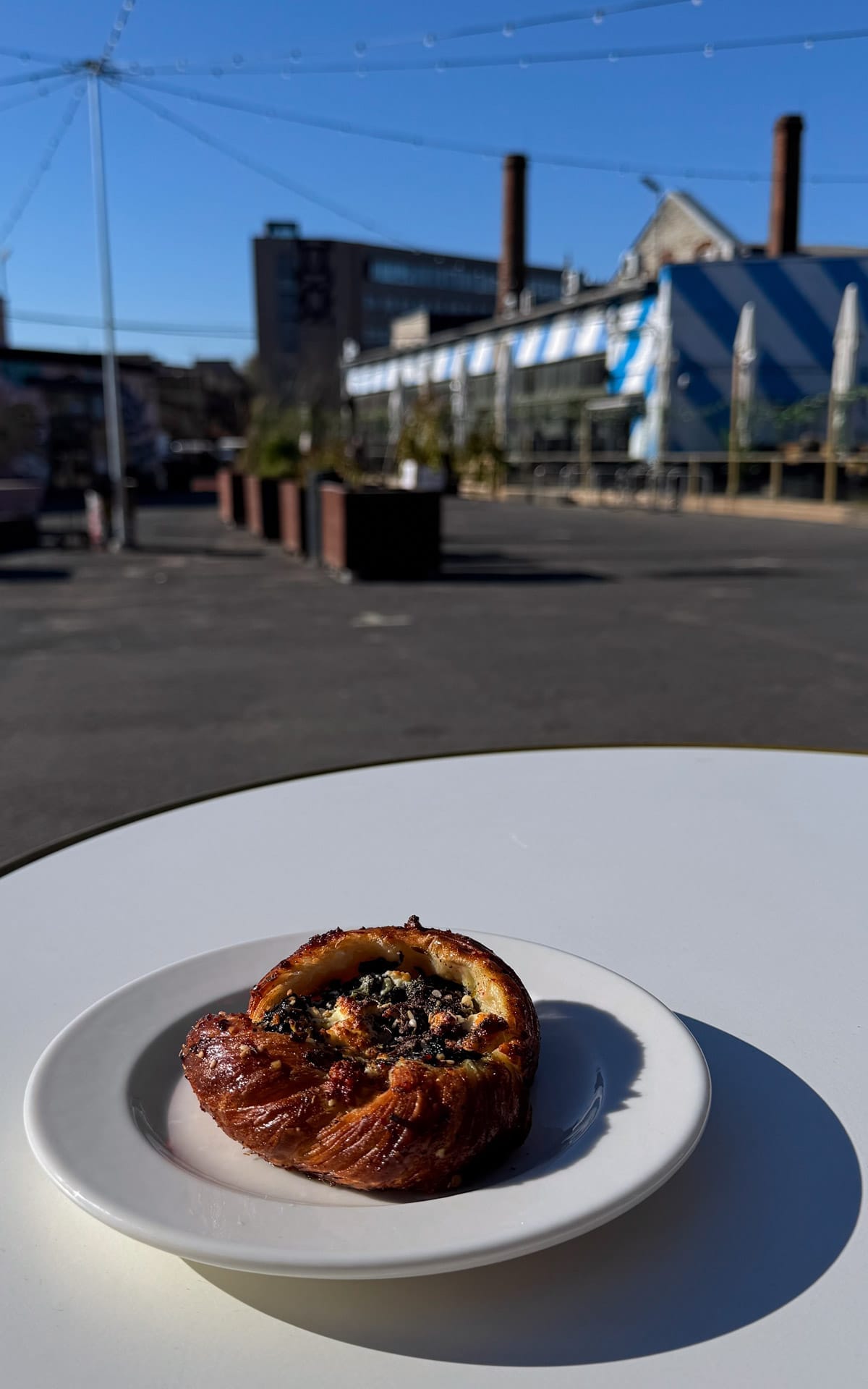 Pastry on a white plate at an outdoor cafe table in Telliskivi Creative City, with industrial buildings in the background.