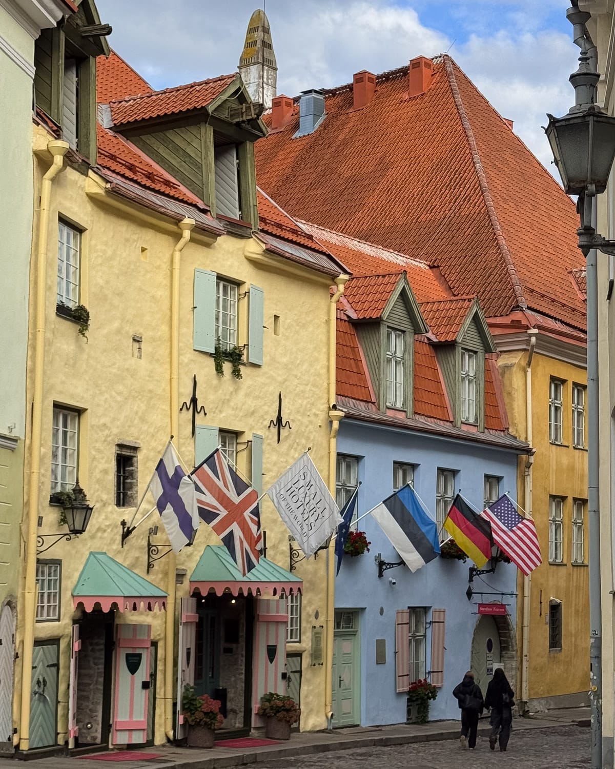 Pastel-coloured medieval buildings and flags of Schlossle Hotel along a cobblestone street in Tallinn’s Old Town.